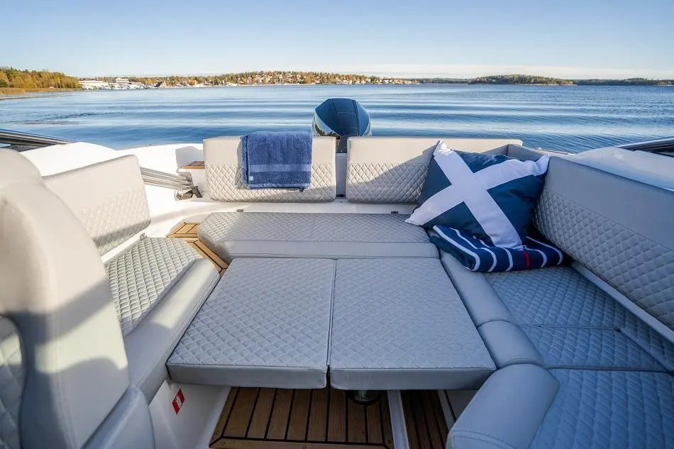 Luxurious boat seating area with a blue towel and decorative cushions, overlooking a calm waterway and trees in the distance.
